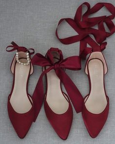 two pairs of red high heeled shoes with a bow tied around the ankle and pearls on each shoe