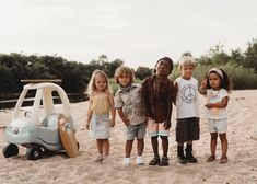 four children standing in front of a toy car on the beach