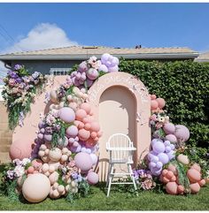 a chair sitting in front of a pink wall with balloons and flowers on the side