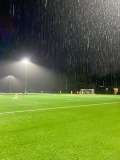 a soccer field at night with the lights on and rain falling from the sky over it