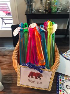 a basket filled with lots of different colored plastic utensils on top of a wooden table