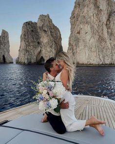 a man and woman sitting on top of a boat in front of some rocks near the ocean