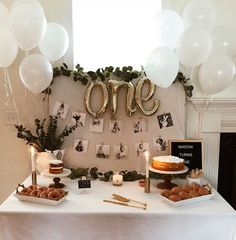 a white table topped with cake and balloons next to a sign that says one on it