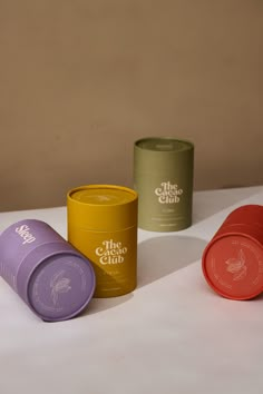 three different colored cups sitting next to each other on top of a white tablecloth