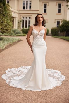 a woman standing in front of a large house wearing a wedding dress with an open back