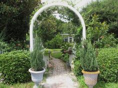 an arch in the middle of a garden with potted plants