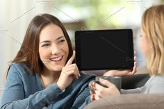 two women sitting on a couch and one is holding up an electronic device to her face