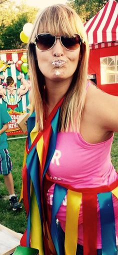 a woman in a pink shirt and some clowns at a carnival with her tongue out