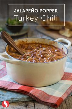 a bowl filled with chili sitting on top of a table next to a wooden spoon