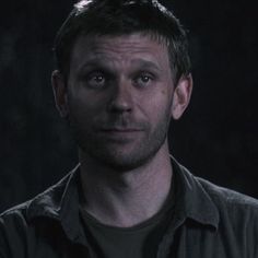 a man looking at the camera with an intense look on his face, in front of a dark background