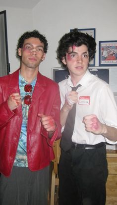 two young men standing next to each other wearing red leather jackets and ties, one with his fist raised