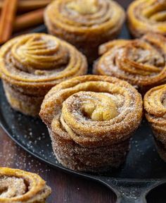 cinnamon rolls on a black plate with cinnamon sticks in the background and powdered sugar sprinkled on top