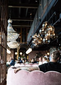 a man sitting on top of a pink couch in a room filled with chandeliers