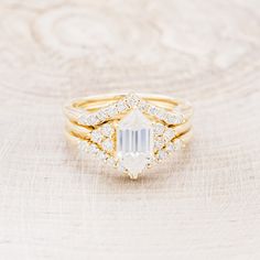 a gold ring with an emerald stone surrounded by diamonds on a wooden surface in front of a white background