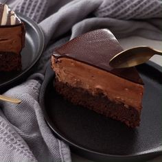 two slices of chocolate cheesecake on black plates with gold serving utensils next to them