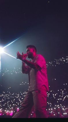 a man standing on top of a stage with his hands in the air and lights behind him