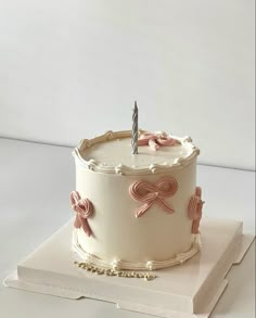 a white cake with pink bows and a single candle sitting on top of a book