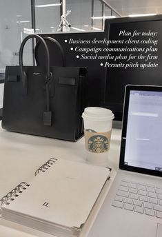 a laptop computer sitting on top of a desk next to a bag and coffee cup