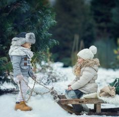 two children are playing in the snow on a sled and one is wearing a hat