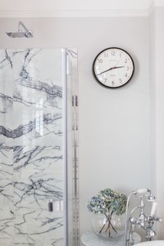 a bathroom with a clock on the wall next to a bathtub and shower stall