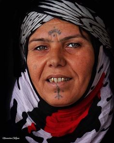 an older woman with tattoos on her face and headdress is looking at the camera