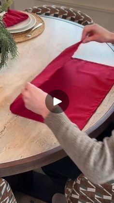 a woman is making a red cloth on a wooden table with other people around it