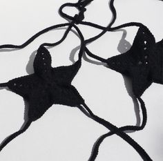 two black crocheted pieces of clothing on a white surface with one string connected to the other