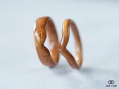 two wooden wedding rings made to look like they are bent in the same direction, on a white surface