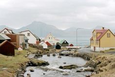 a river running through a small town with mountains in the background and houses on either side