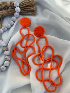 an orange pair of earrings is laying on a white cloth next to a beaded necklace