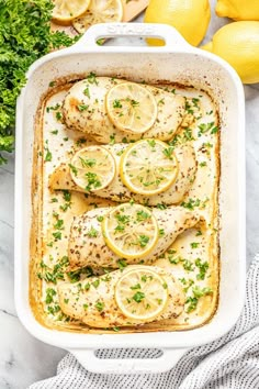 baked chicken with lemons and parsley in a white casserole dish on a marble surface