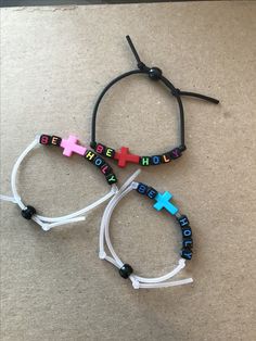 three bracelets with colorful crosses and words on them sitting on the floor next to each other