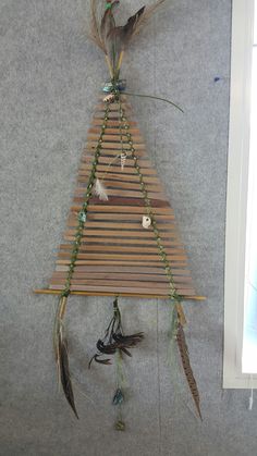 a wooden structure with feathers hanging from it's sides and beads on the top