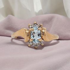 This 10k yellow gold ring features a .40-carat oval Aquamarine as its centerpiece accented elegantly with Diamonds positioned above and below the center stone. The Aquamarine, known for its tranquil blue hue, is complemented by the sparkling brilliance of the Diamonds, adding a touch of sophistication and contrast to the overall design. This combination creates a timeless and eye-catching piece of jewelry, perfect for someone who appreciates both elegance and understated luxury.   Free resizing Oval Topaz Ring With Center Stone For Formal Occasions, Formal Oval Cluster Ring With Center Stone, Gold Marquise Topaz Ring For Anniversary, Classic Yellow Gold Topaz Ring With Diamond Accents, Classic Topaz Ring With Diamond Accents, Oval Heirloom Topaz Ring For Formal Occasions, Oval Diamond Cut Topaz Ring For Anniversary, Oval Diamond Ring With Accent Stones For Formal Events, Oval Diamond Ring With Accent Stones For Formal Occasions