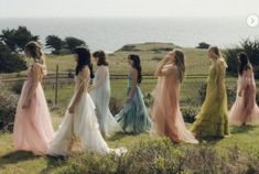 a group of women walking across a lush green field next to the ocean on top of a hill