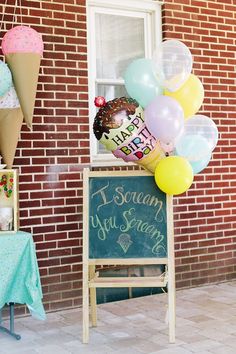 an ice cream parlor with balloons and birthday cake on the sign in front of it