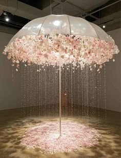 an umbrella with flowers hanging from it in the middle of a room filled with pink petals