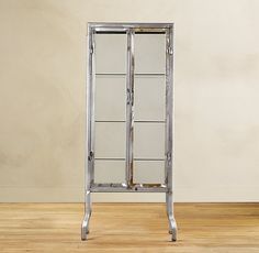 a tall mirrored cabinet sitting on top of a wooden floor next to a white wall