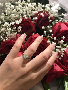 a woman's hand with a diamond ring on her finger next to red roses