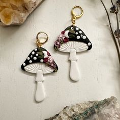 two white and black mushrooms with flowers on them are hanging from gold - plated hooks