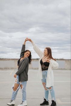 two young women standing next to each other in an empty parking lot with their arms up