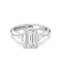 an emerald cut diamond ring with three side stones on the band and shoulders, set in 18k white gold