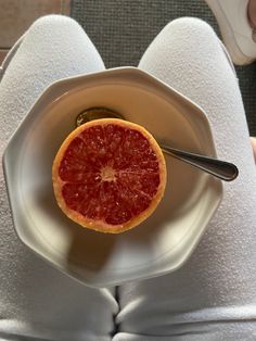 a grapefruit cut in half on a white plate with a spoon and napkin