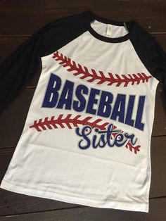 a baseball shirt with the word baseball sister on it sitting on top of a wooden floor