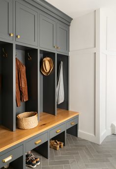 an entryway with gray cabinets and wooden bench, hat hanging on coat rack in the corner