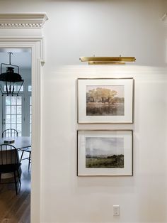 three paintings hang on the wall in a room with white walls and wood flooring