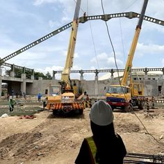 some construction workers are standing in front of two large cranes and one is working on the ground