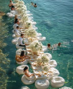 several people are sitting on inflatable chairs and floating flowers along the water's edge