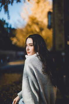 a woman sitting on the ground with her hair blowing in the wind and wearing a white sweater