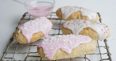 three donuts with pink icing and sprinkles on a cooling rack